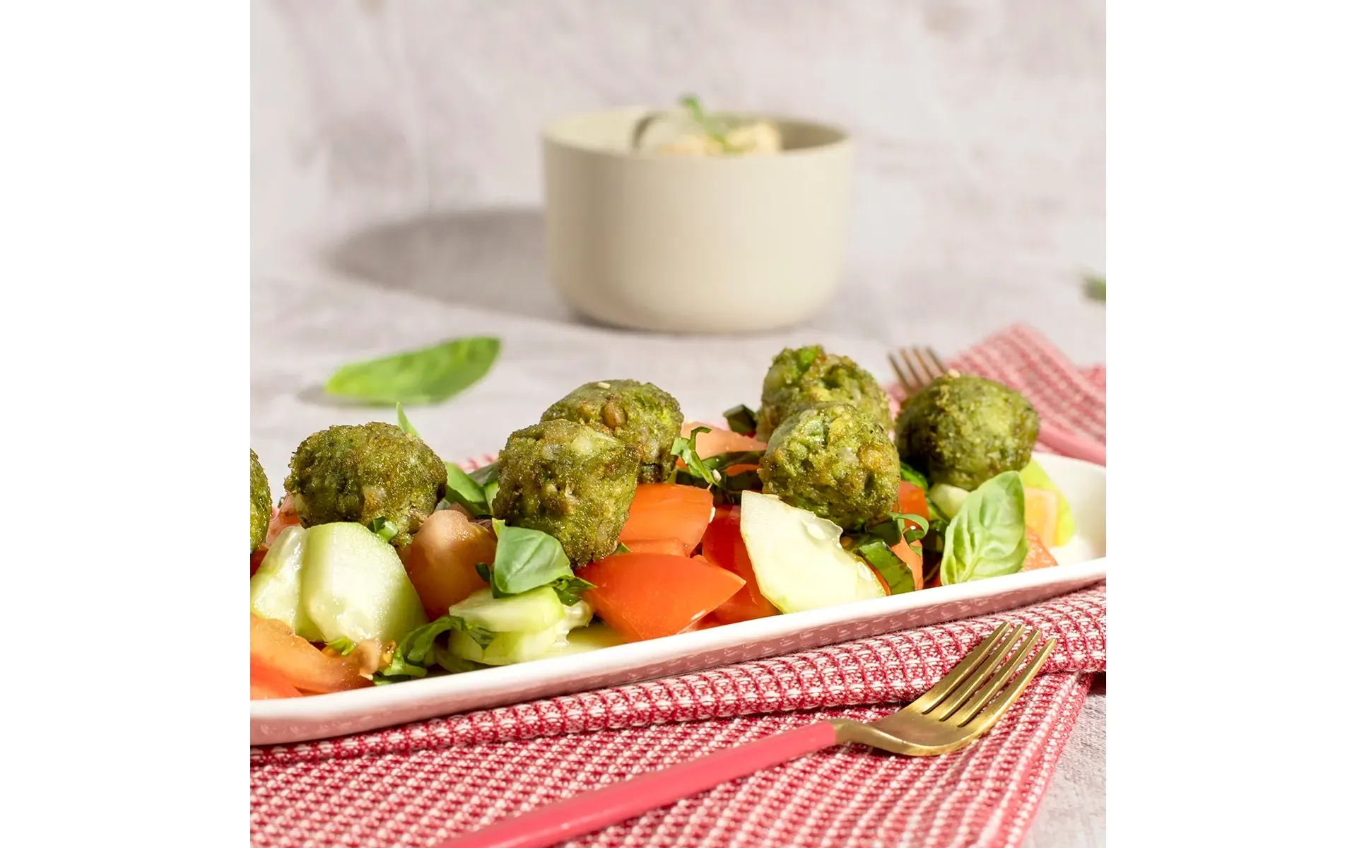 Piatto con hummus cremoso Orogel, accompagnato da polpettine vegetariane e verdure fresche, con forchetta.