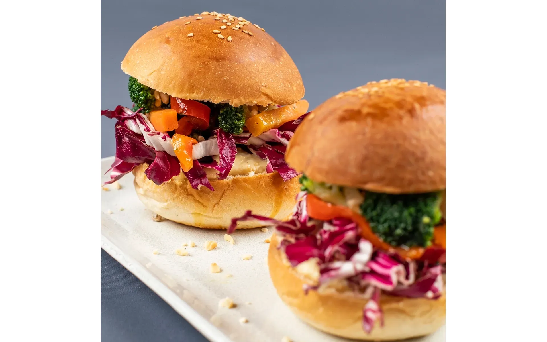 Due sfiziosi miniburger con verdure fresche e formaggio filante, serviti su un elegante piatto bianco.