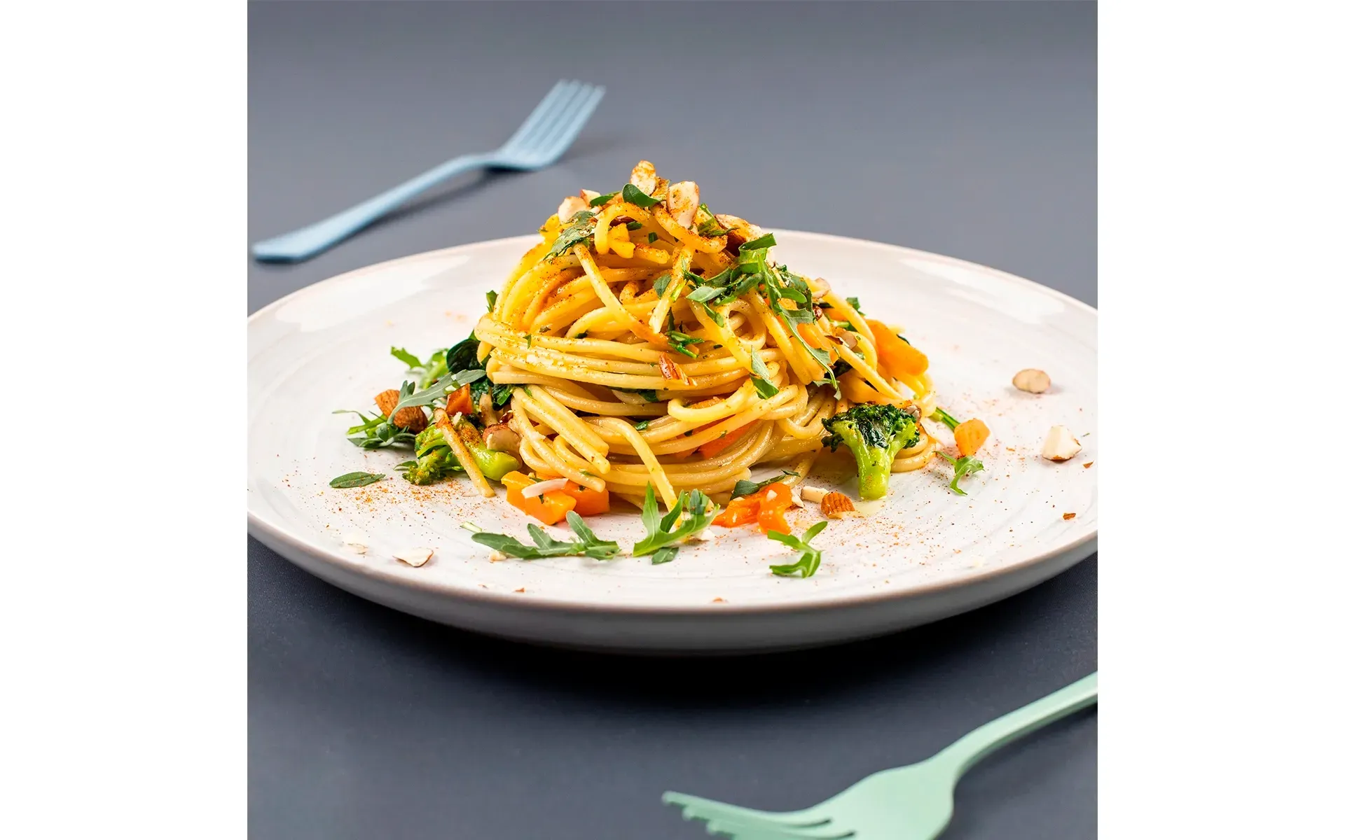 Piatto di spaghettoni Orogel conditi con verdure fresche, mandorle croccanti, paprika dolce e rucola.