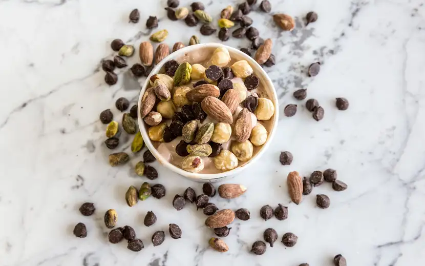Mandorle e nocciole: scopri le proprietà della frutta secca. Ciotola con noci e semi su marmo.