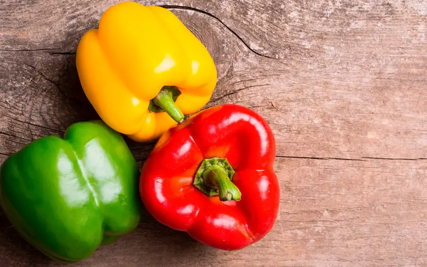 Un pieno di vitamina A e C: viva i peperoni! Tre peperoni colorati su un tavolo di legno.