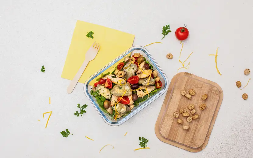 Idee per la pausa pranzo: cosa mangiare? Contenitore take-away con verdure fresche su tagliere.