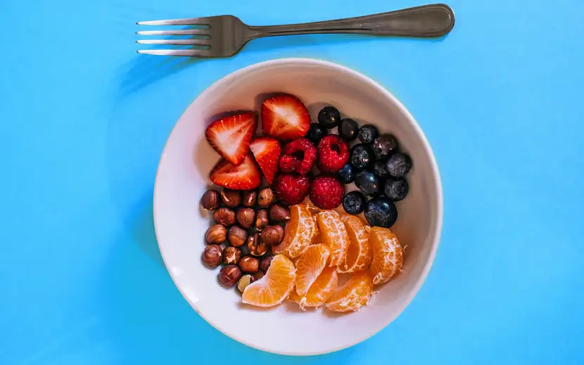 Cosa mangiare a merenda? Una ciotola colorata di frutta fresca e noci, per uno spuntino sano.