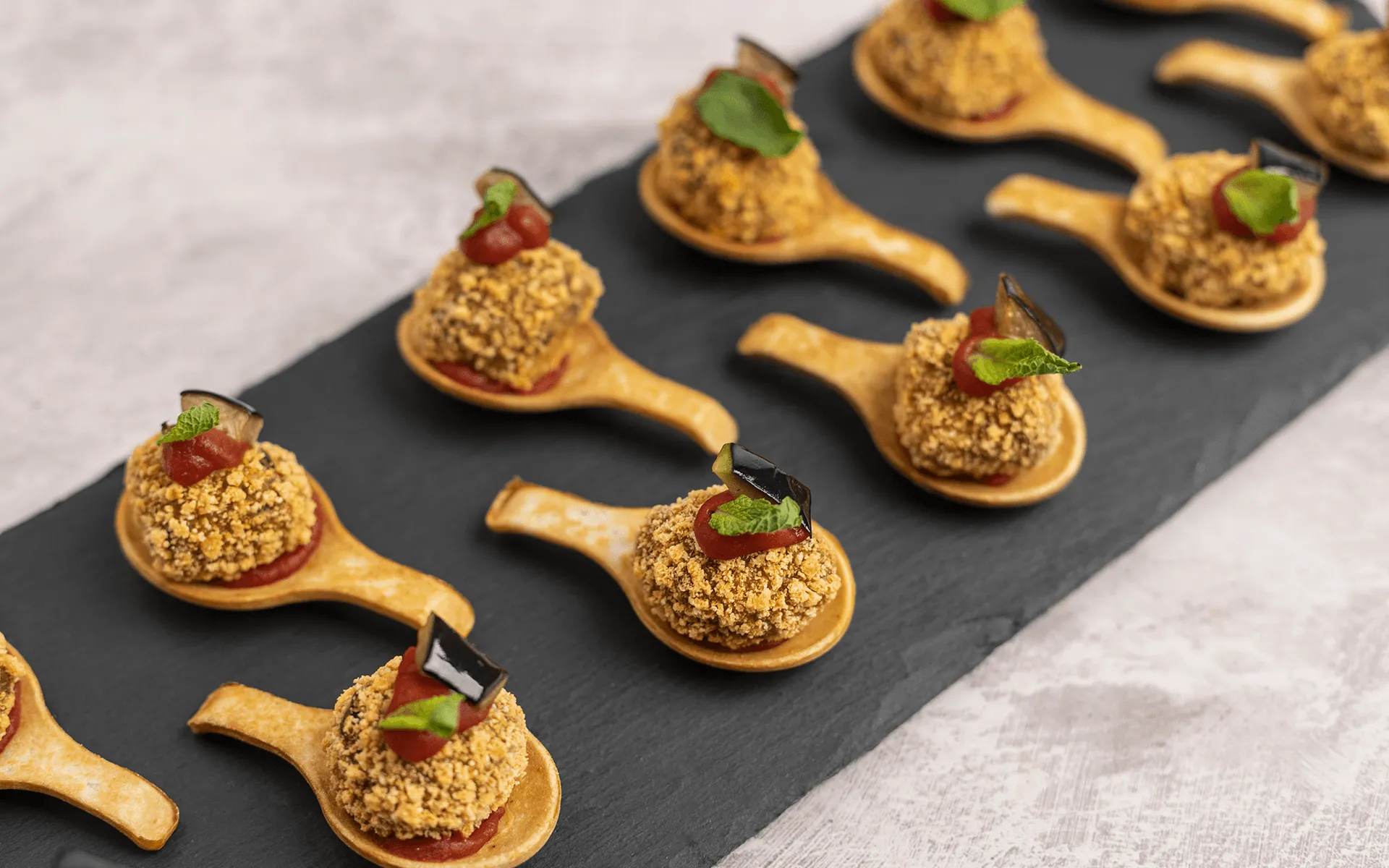 Piccoli stuzzichini gourmet disposti con cura su una lavagna nera, per un buffet elegante.