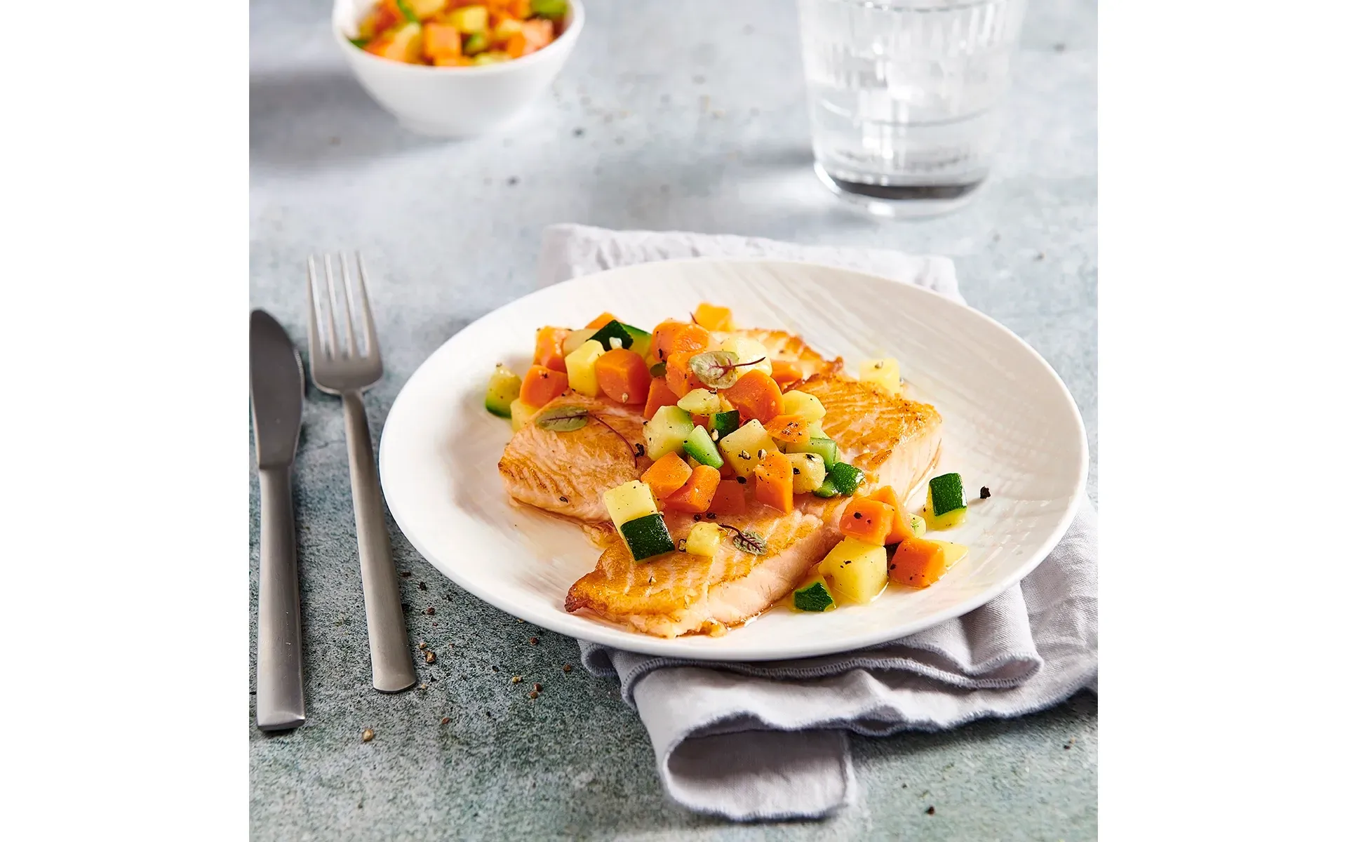 L'immagine mostra un filetto di salmone in padella con contorno di verdure.