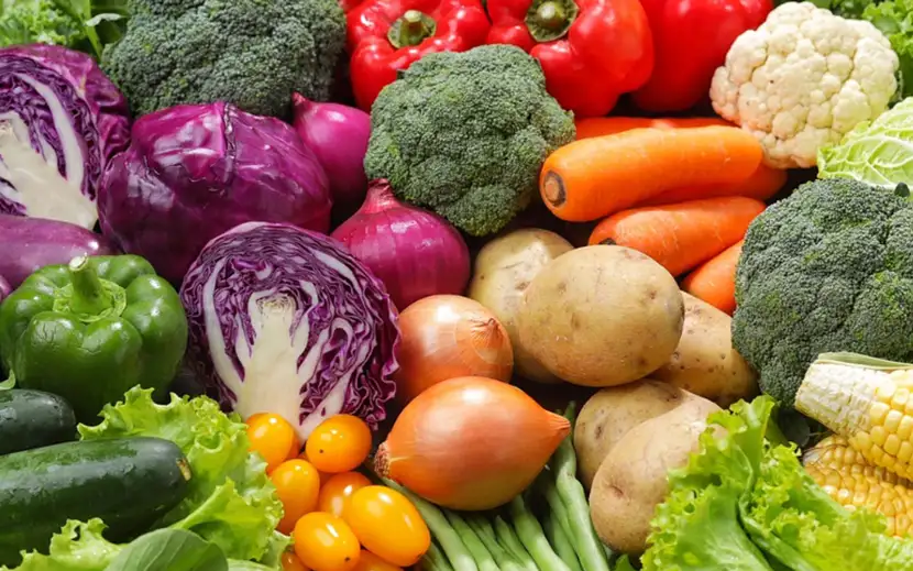 Verdura dei 5 colori del benessere disposte su un piano: broccoli, lattuga, carote, cavolo viola, cipolle, pomodori, peperoni e patate.