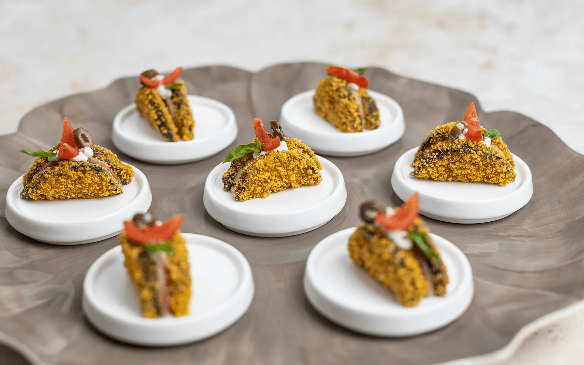 Elegante piatto da portata con una selezione di finger food Orogel in piccoli piattini bianchi.