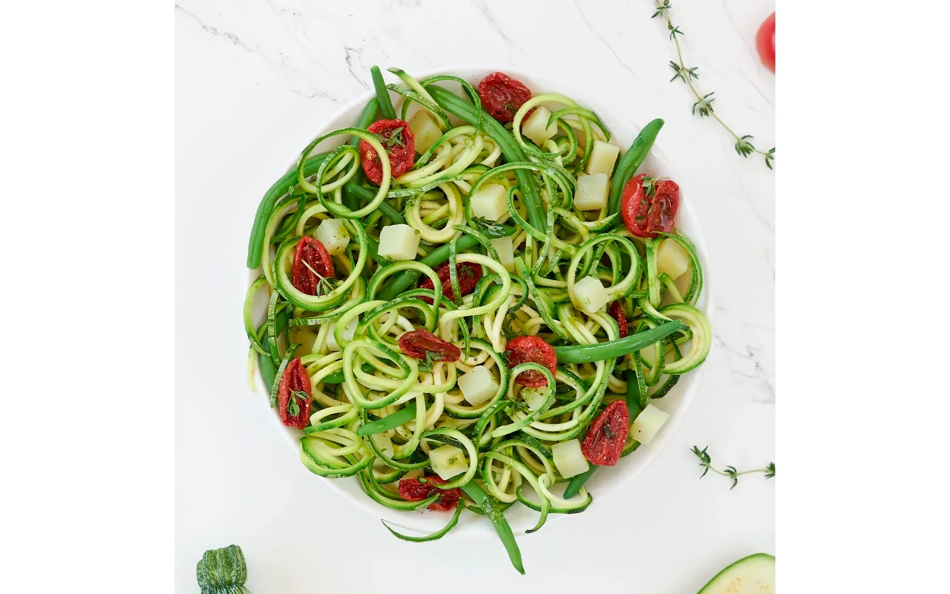 Ciotola di spaghetti di zucchine conditi con pesto, fagiolini, patate e pomodorini freschi.