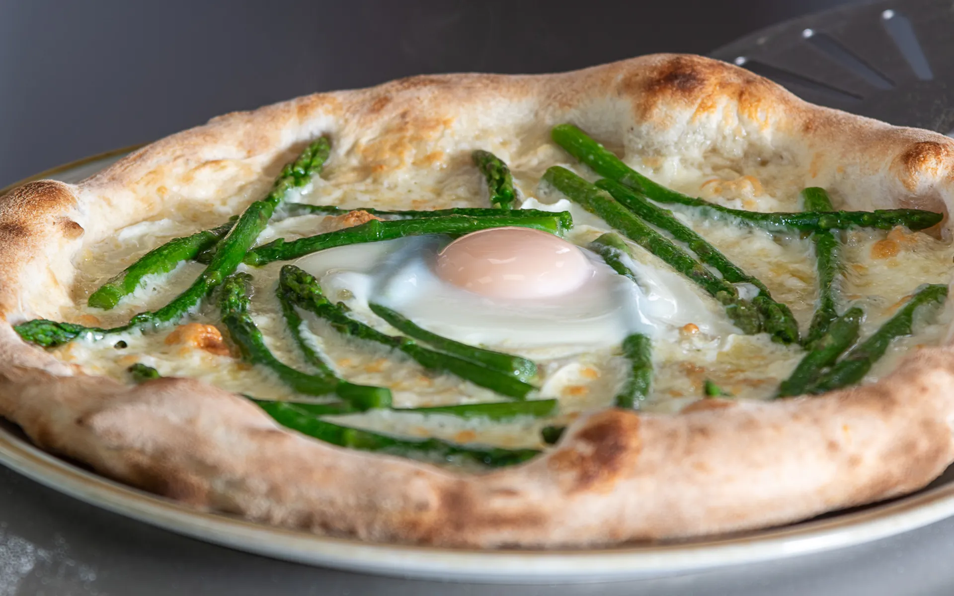 Pizza contemporanea con uovo al centro, asparagi verdi e mozzarella fior di latte, appena sfornata.