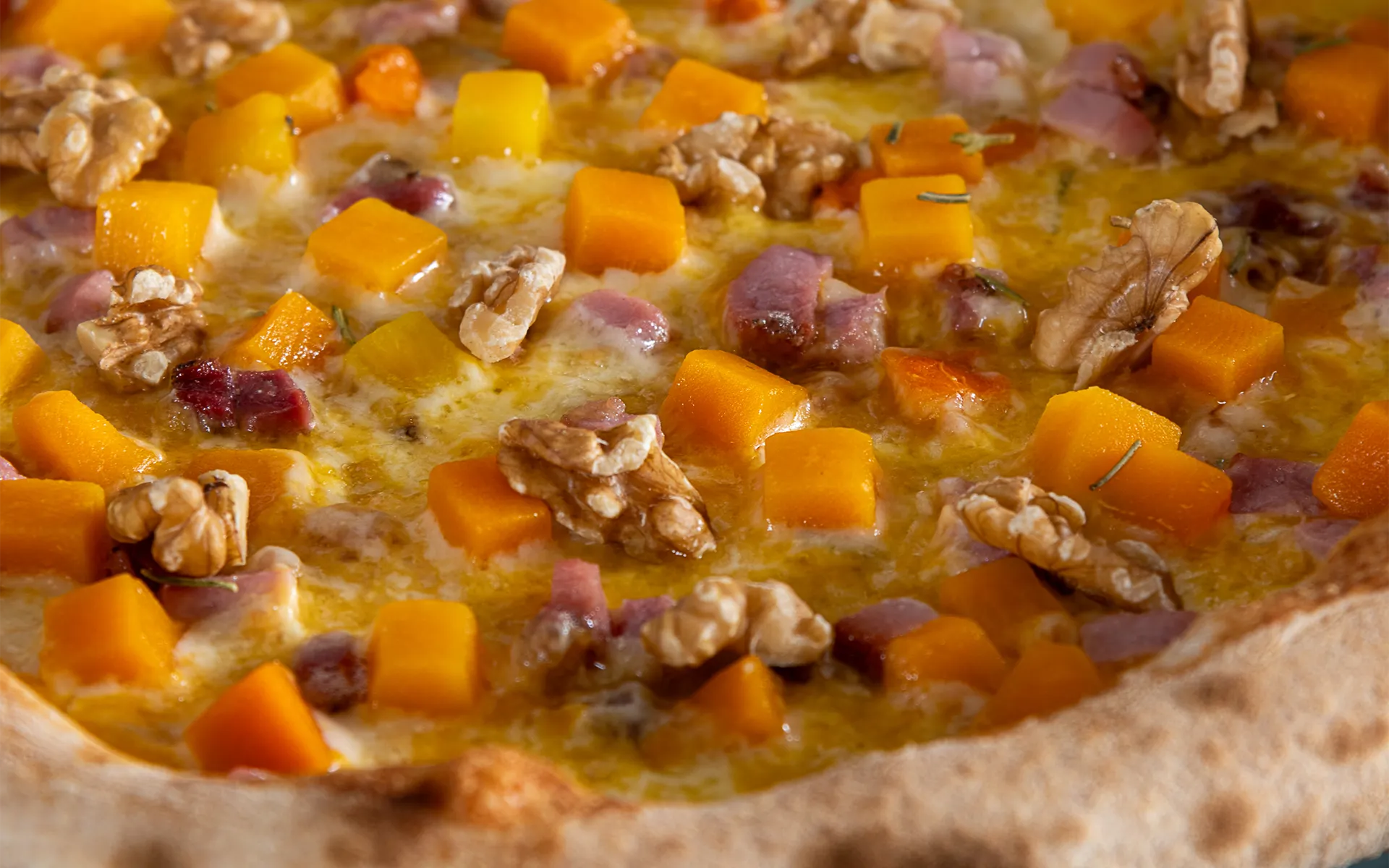 Pizza tonda con zucca a cubetti, speck, pancetta affumicata, rosmarino e noci, dal gusto intenso e avvolgente.