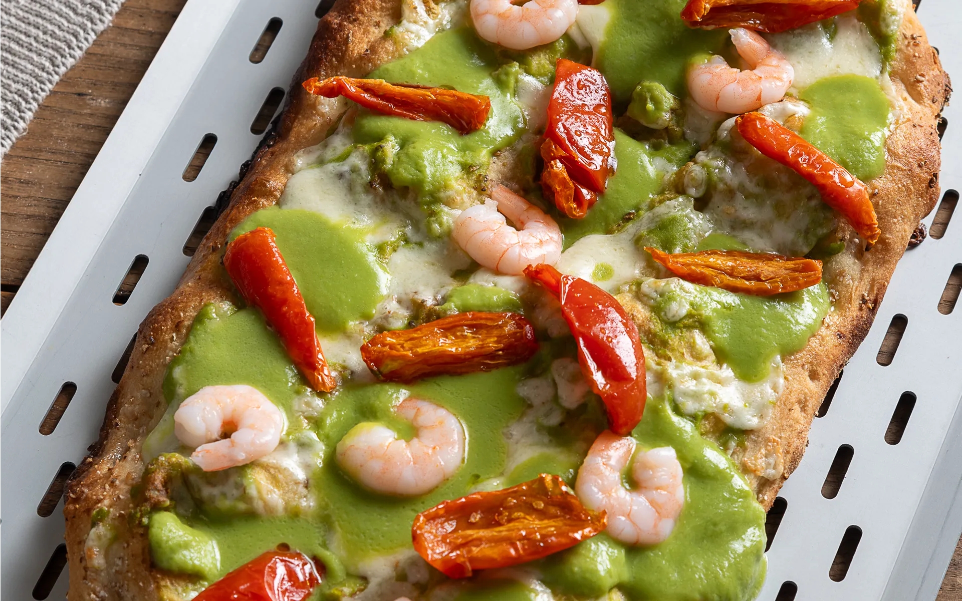 Pizza alla pala con purea di piselli, pomodori semi dry e gamberetti, dal gusto fresco e bilanciato.