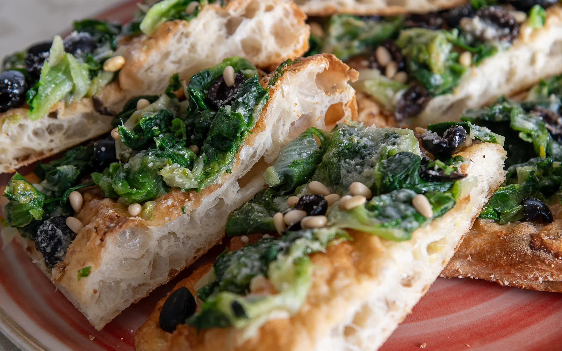 Pizza in teglia con scarola, parmigiano grattugiato, olive nere e pinoli, dal gusto ricco e mediterraneo.