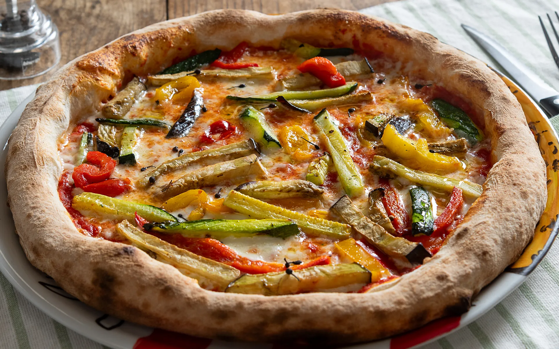 Pizza tonda classica con pomodoro, mozzarella filante e verdure grigliate, dal gusto mediterraneo e profumato.