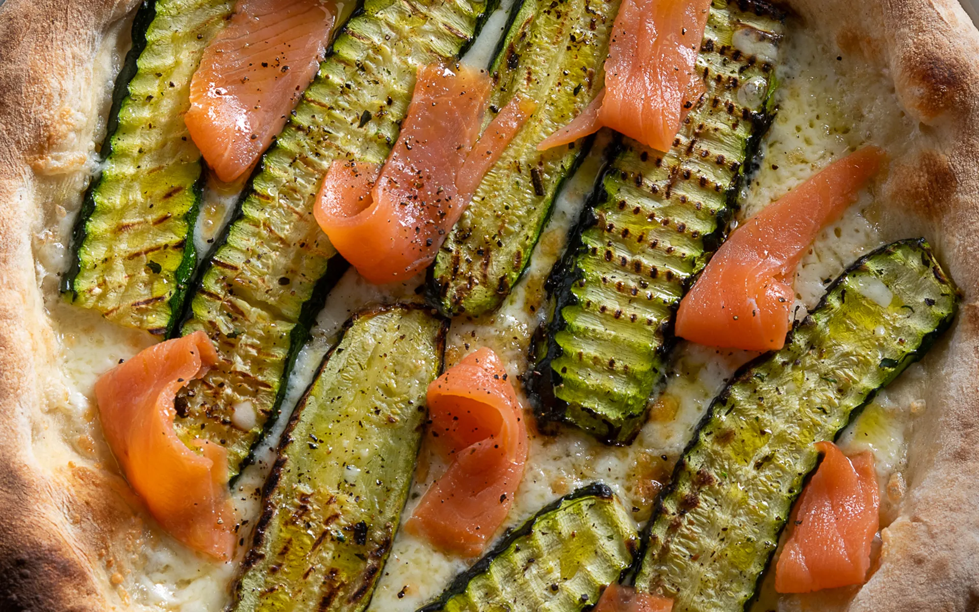 Pizza tonda classica con mozzarella filante, zucchine grigliate e salmone affumicato, dal gusto delicato e raffinato.