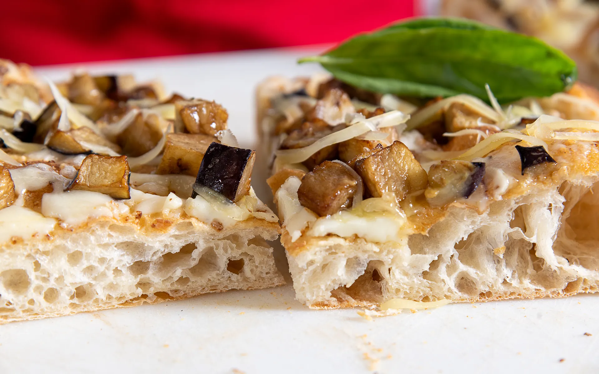 Pizza in teglia con mozzarella filante e melanzane, dorata e soffice alla vista.