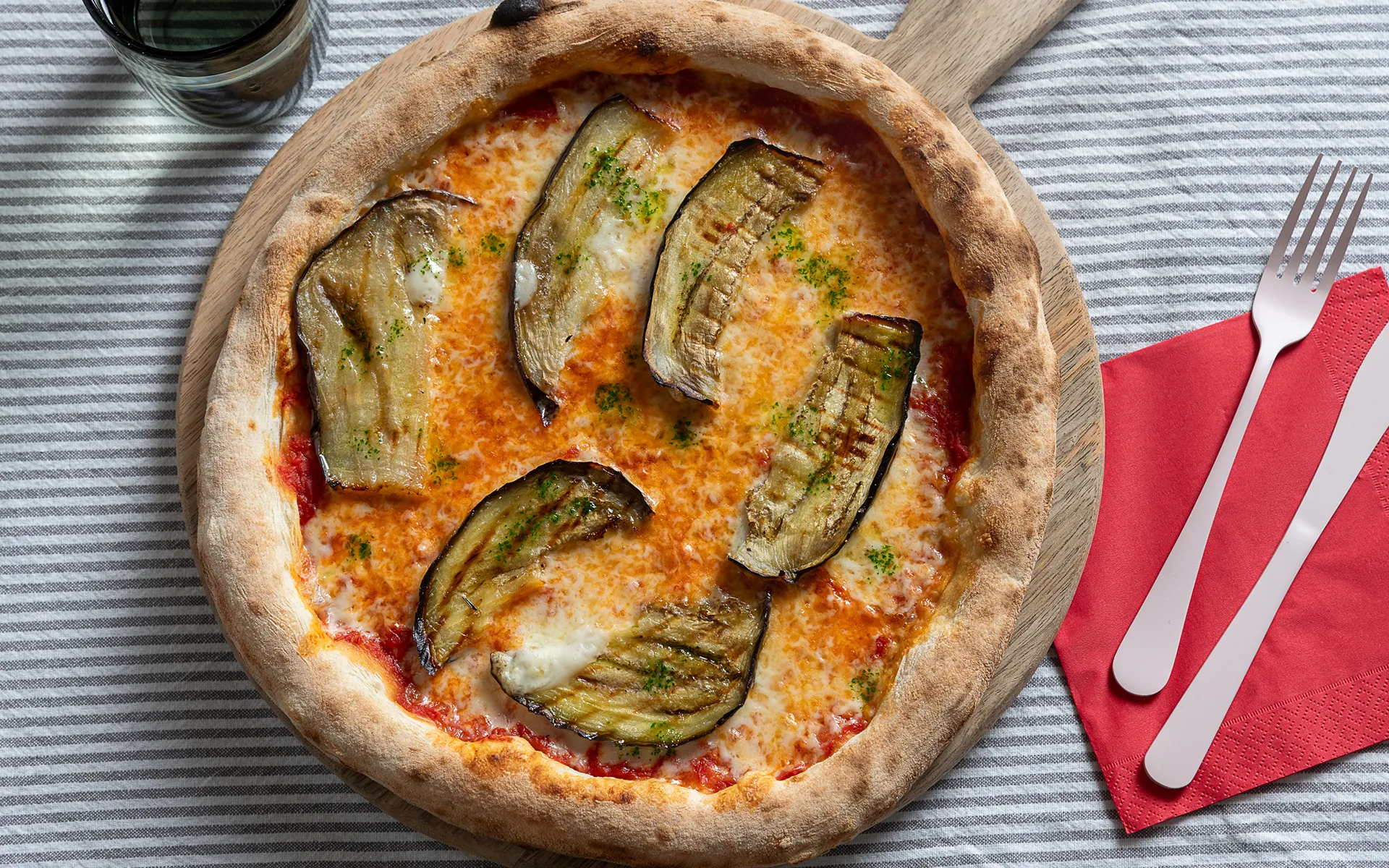 Pizza tonda con pomodoro, mozzarella filante e melanzane a fette per parmigiana, dal gusto ricco e mediterraneo.