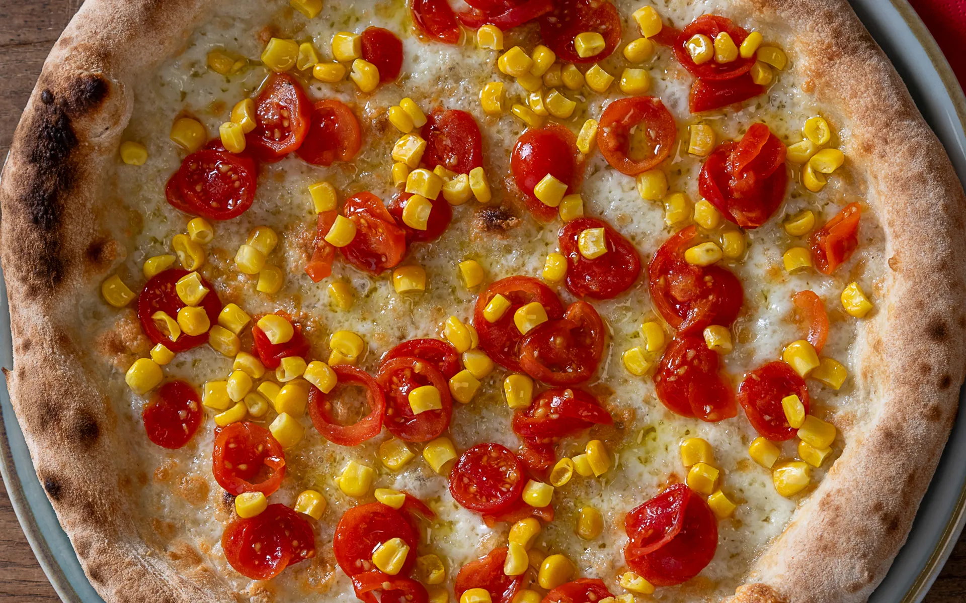 Pizza tonda con mozzarella filante, pomodorini e mais, dal gusto fresco e delicato.