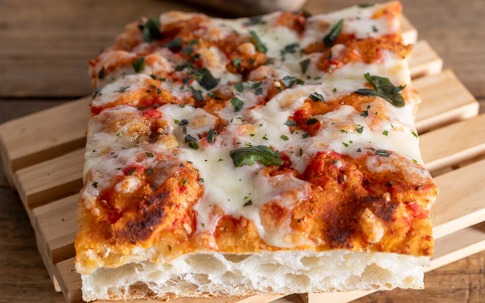 Pizza in teglia con pomodoro, mozzarella filante e basilico fresco, dal profumo classico e mediterraneo.