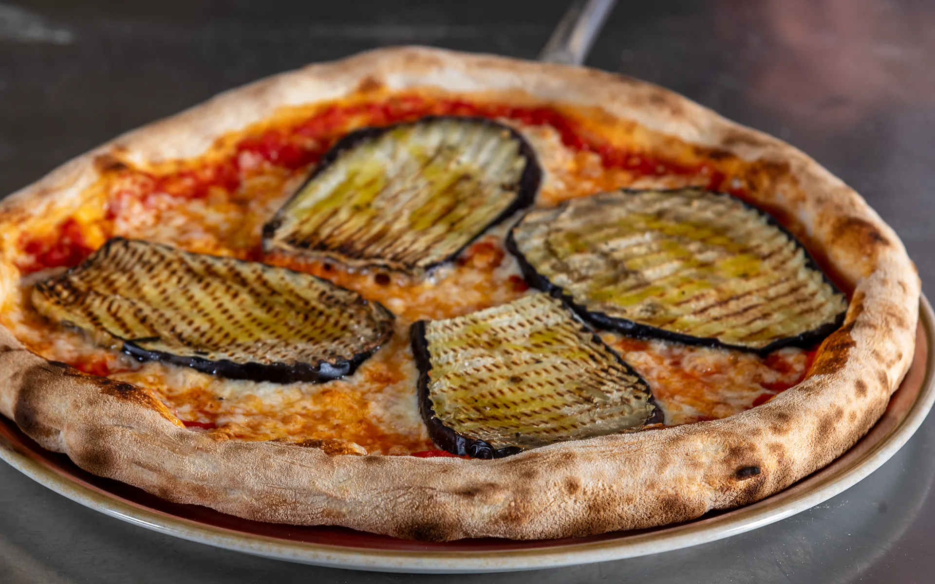 Pizza tonda con pomodoro, mozzarella filante e melanzane grigliate, dal gusto equilibrato e mediterraneo.