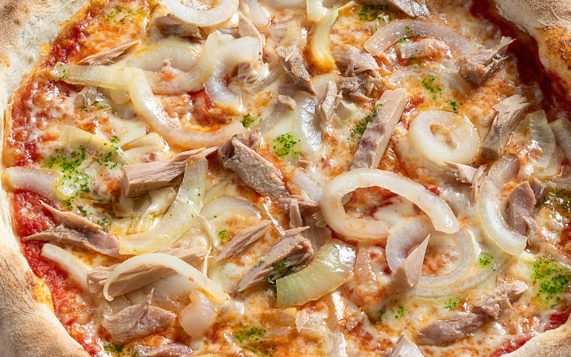 Pizza tonda classica con pomodoro, mozzarella filante, cipolla a fette e tonno, dal gusto deciso e mediterraneo.