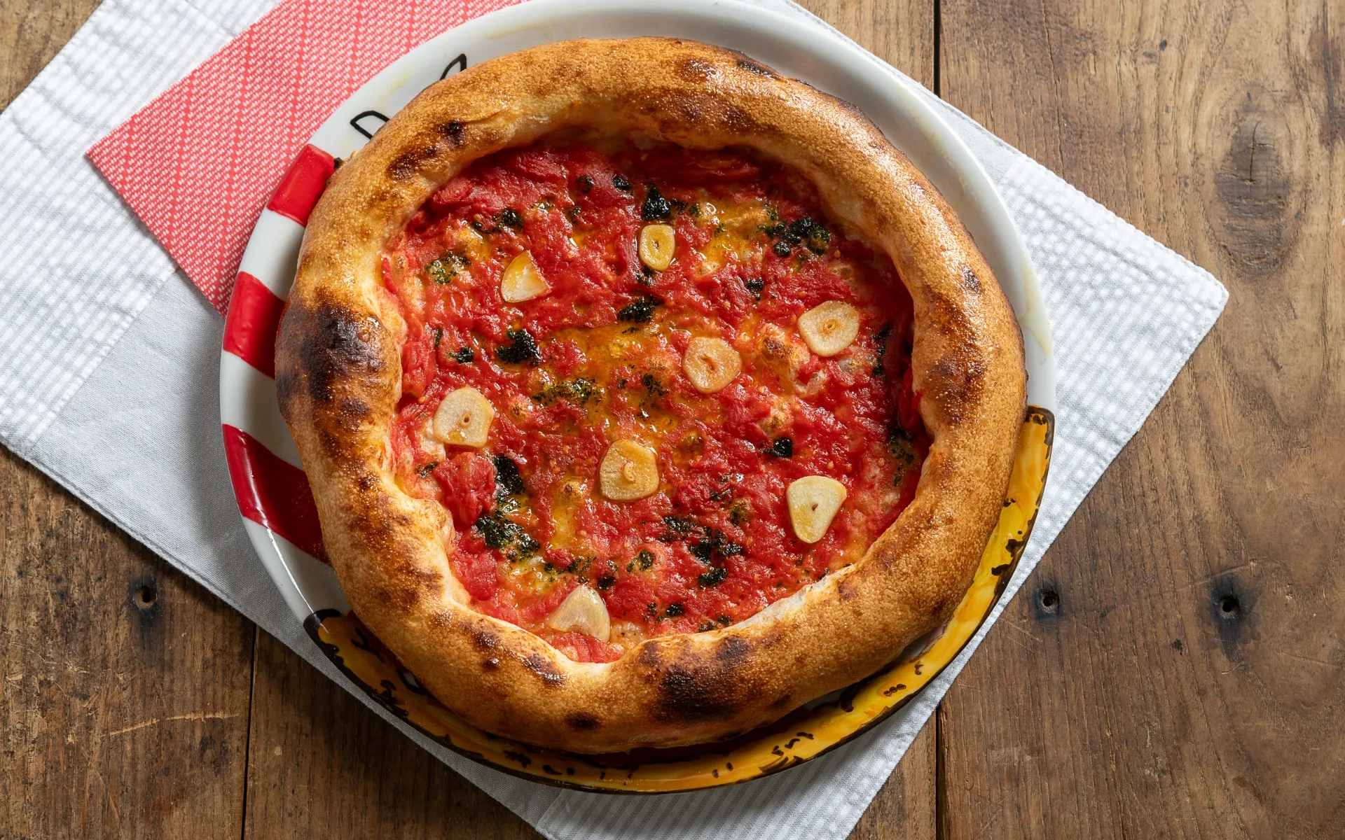 Pizza contemporanea al pomodoro con aglio e prezzemolo, condita con olio extravergine di oliva e cotta in forno.