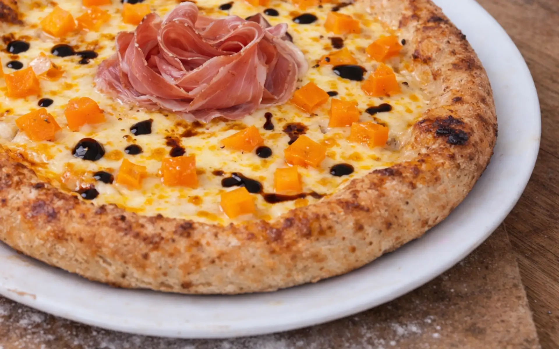 Pizza con purea di zucca, zucca a cubetti, speck e aceto balsamico, dal profilo aromatico equilibrato.