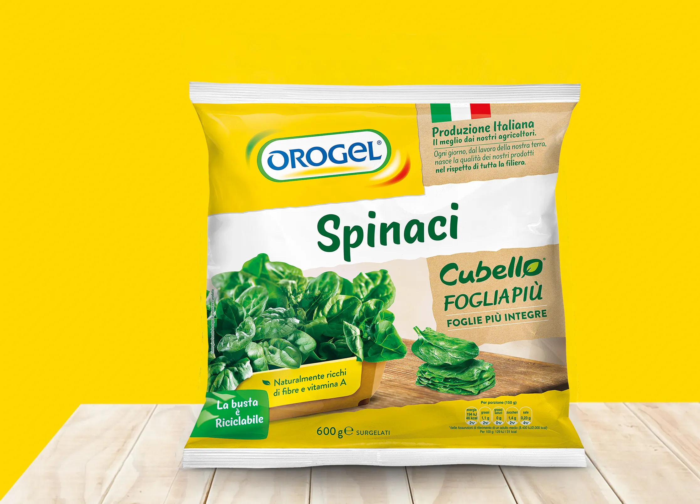 Confezione di spinaci surgelati OROGEL “Spinaci Cubello Fogliapiù” da 600 g, su sfondo giallo con piano in legno; in primo piano foglie di spinaci freschi e indicazioni su produzione italiana e busta riciclabile.