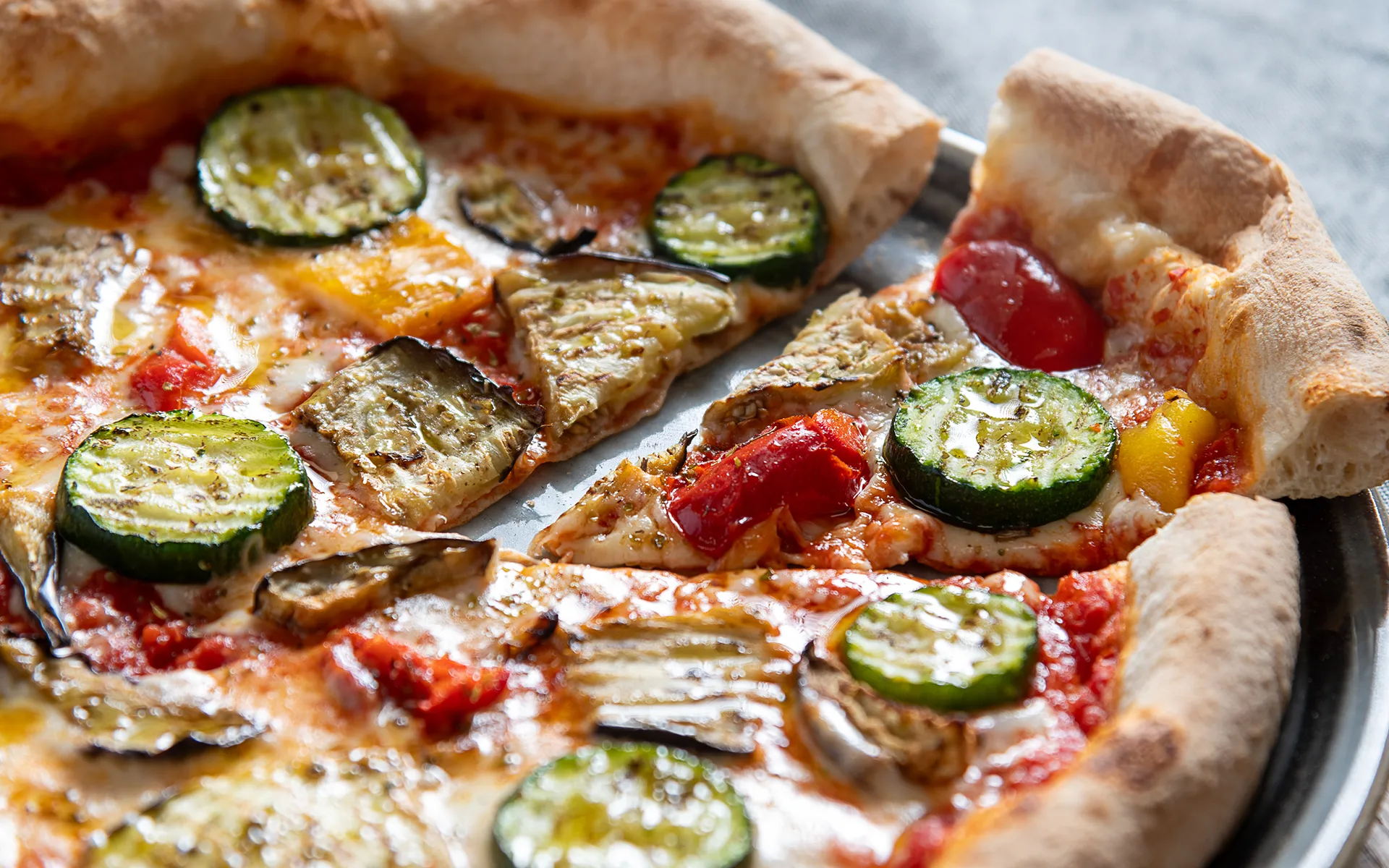Pizza con pomodoro, mozzarella filante e verdure grigliate, dai profumi intensi e dal gusto mediterraneo.