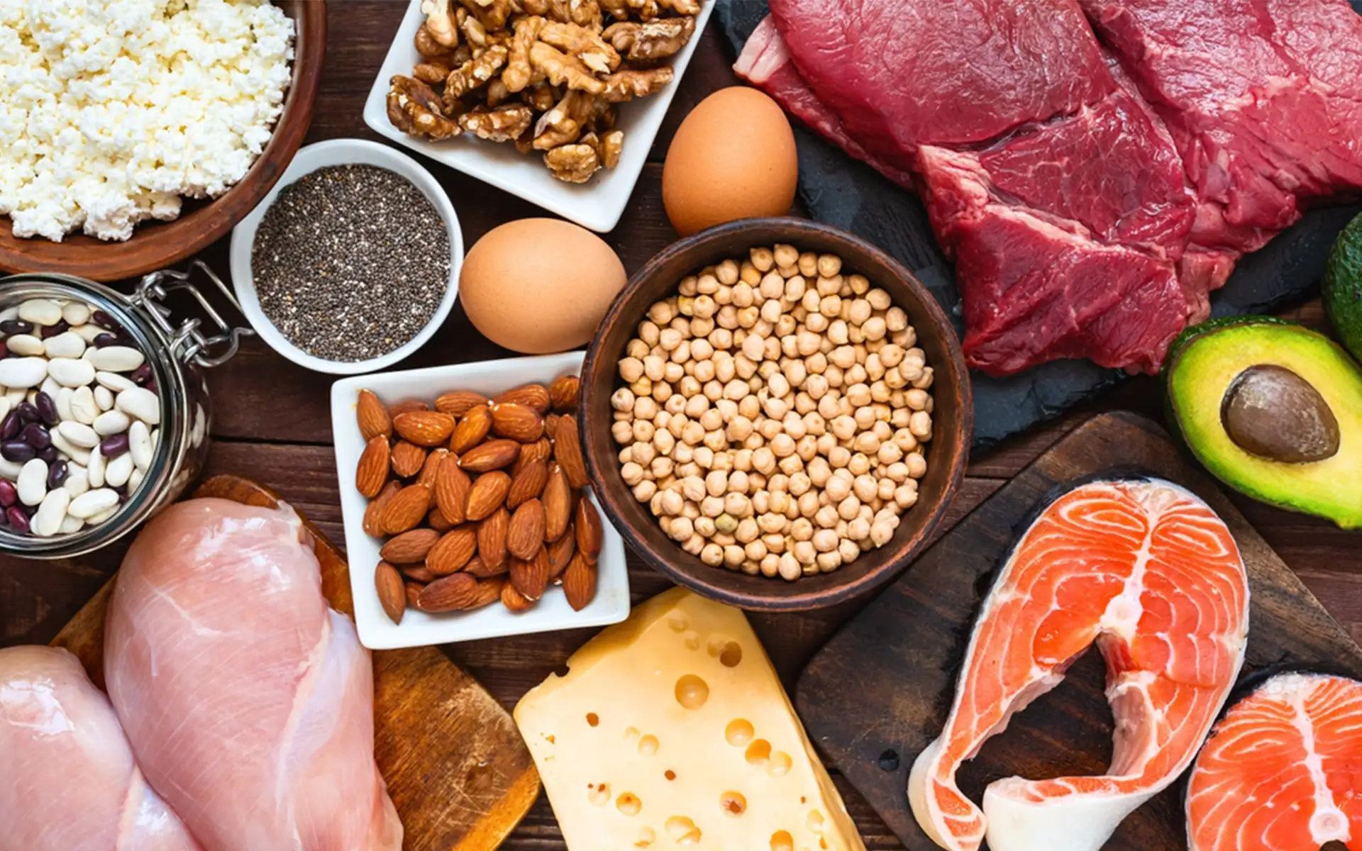 Selezione di alimenti proteici vegetali con ceci, lenticchie, fagioli, soia edamame, quinoa, avena, broccoli, spinaci, frutta secca, semi e cereali integrali disposti su un piano cucina.