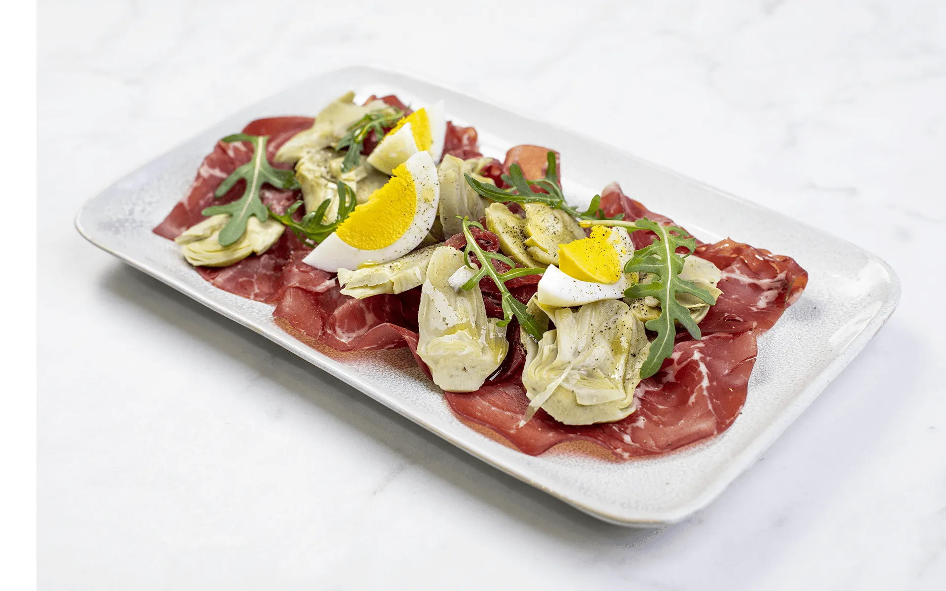 Carciofi Orogel e bresaola: un antipasto leggero e raffinato, servito su un tavolo di marmo.