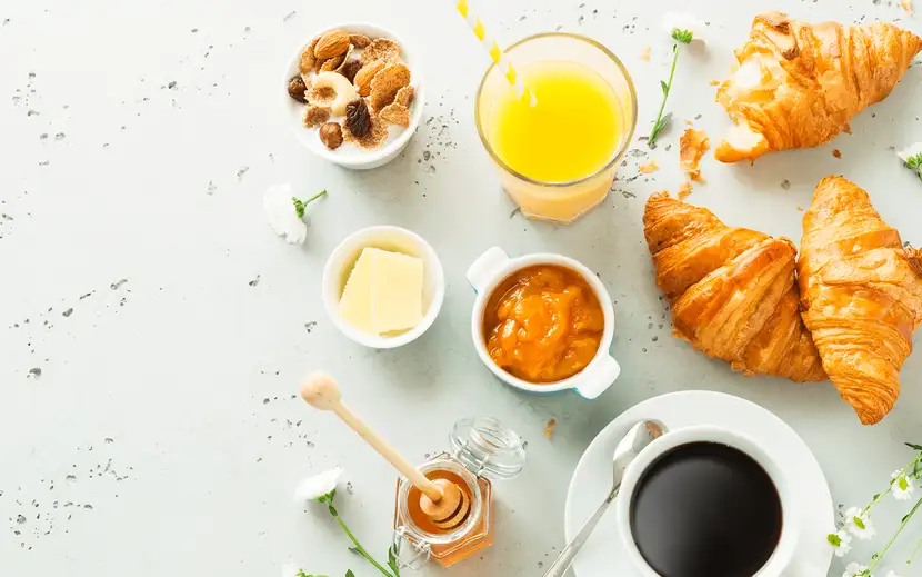 Colazione equilibrata Orogel: tavolo con caffè, croissant e altri prodotti da forno.