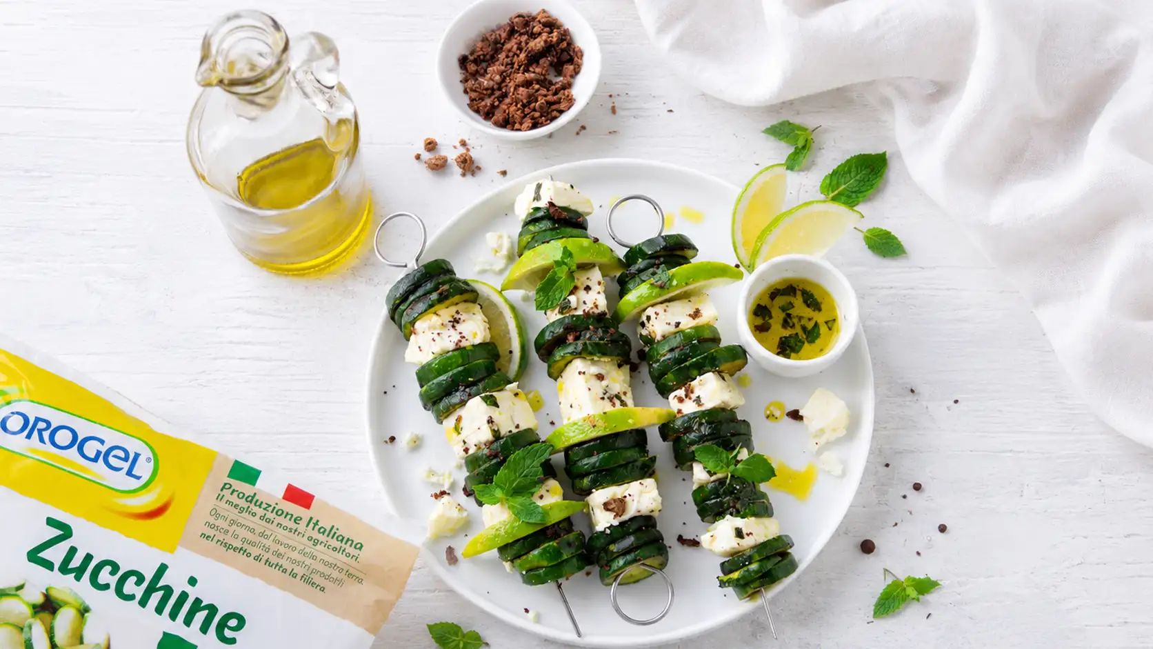 Spiedini di zucchine a fette Orogel con feta, lime e menta, conditi con olio extravergine d'oliva. Ricetta estiva semplice e gustosa preparata con Zucchine a Fette Orogel.