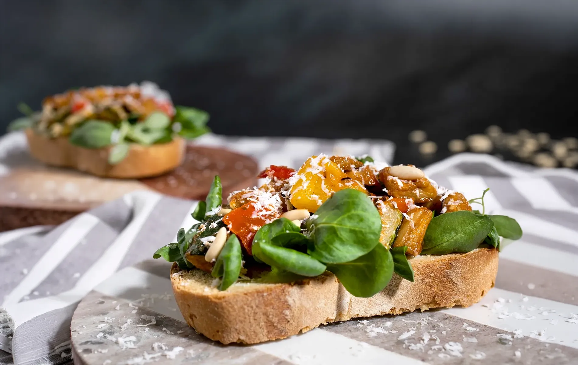 Crostino con caponata di verdure, pinoli, scaglie di formaggio e foglie verdi.