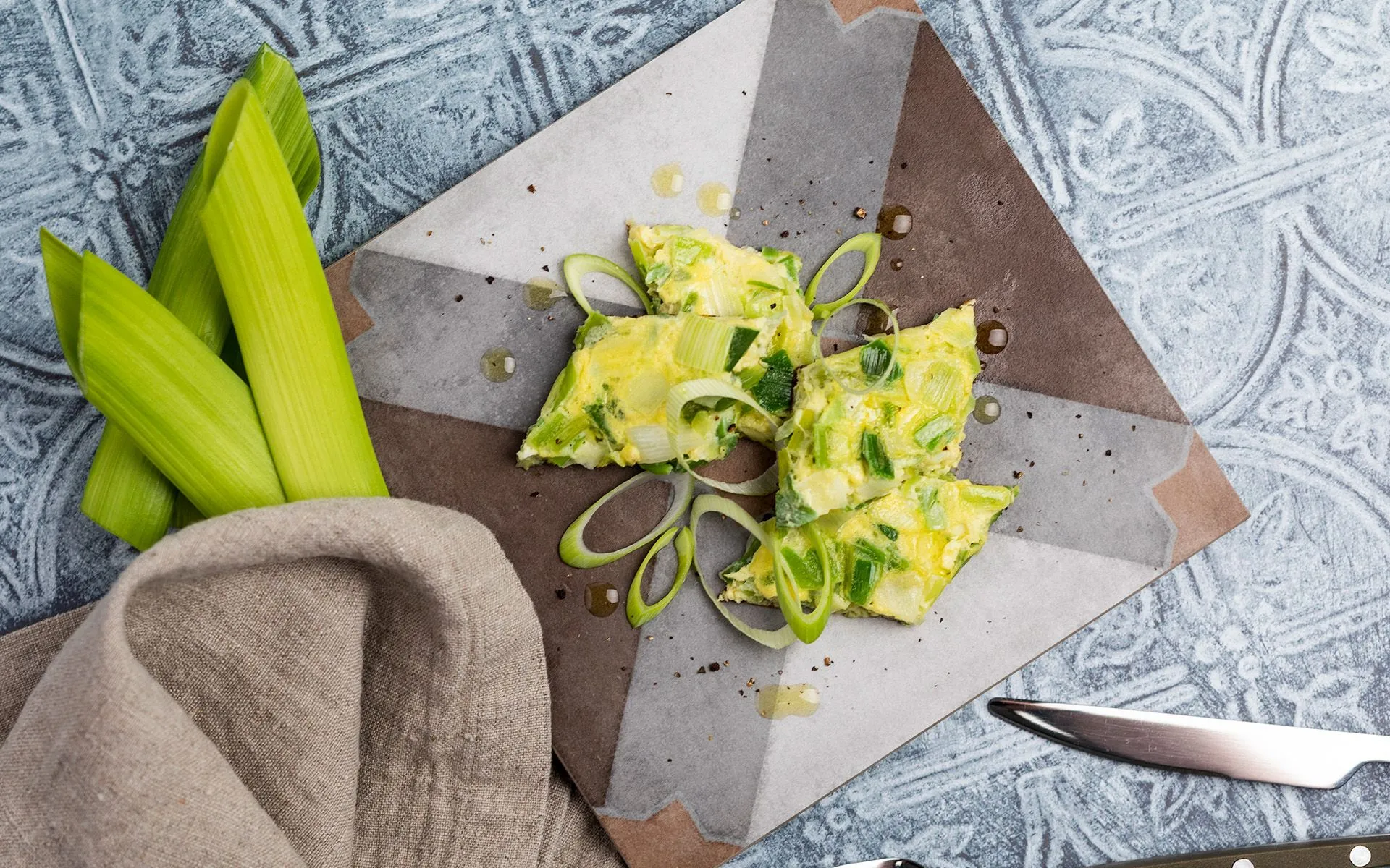 Immagine hero Orogel dedicata al porro: porro fresco, sedano e un coltello su un tavolo.