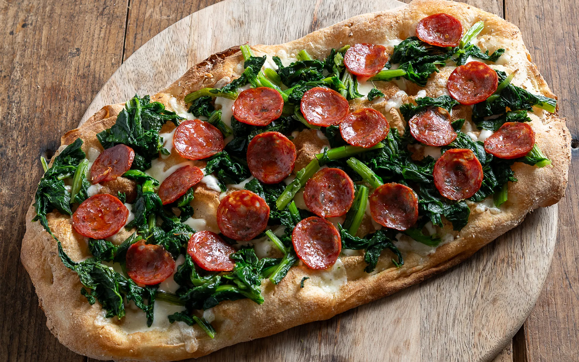 Pizza alla pala con mozzarella filante, cime di rapa e salamino, appena sfornata e servita su pala in legno.