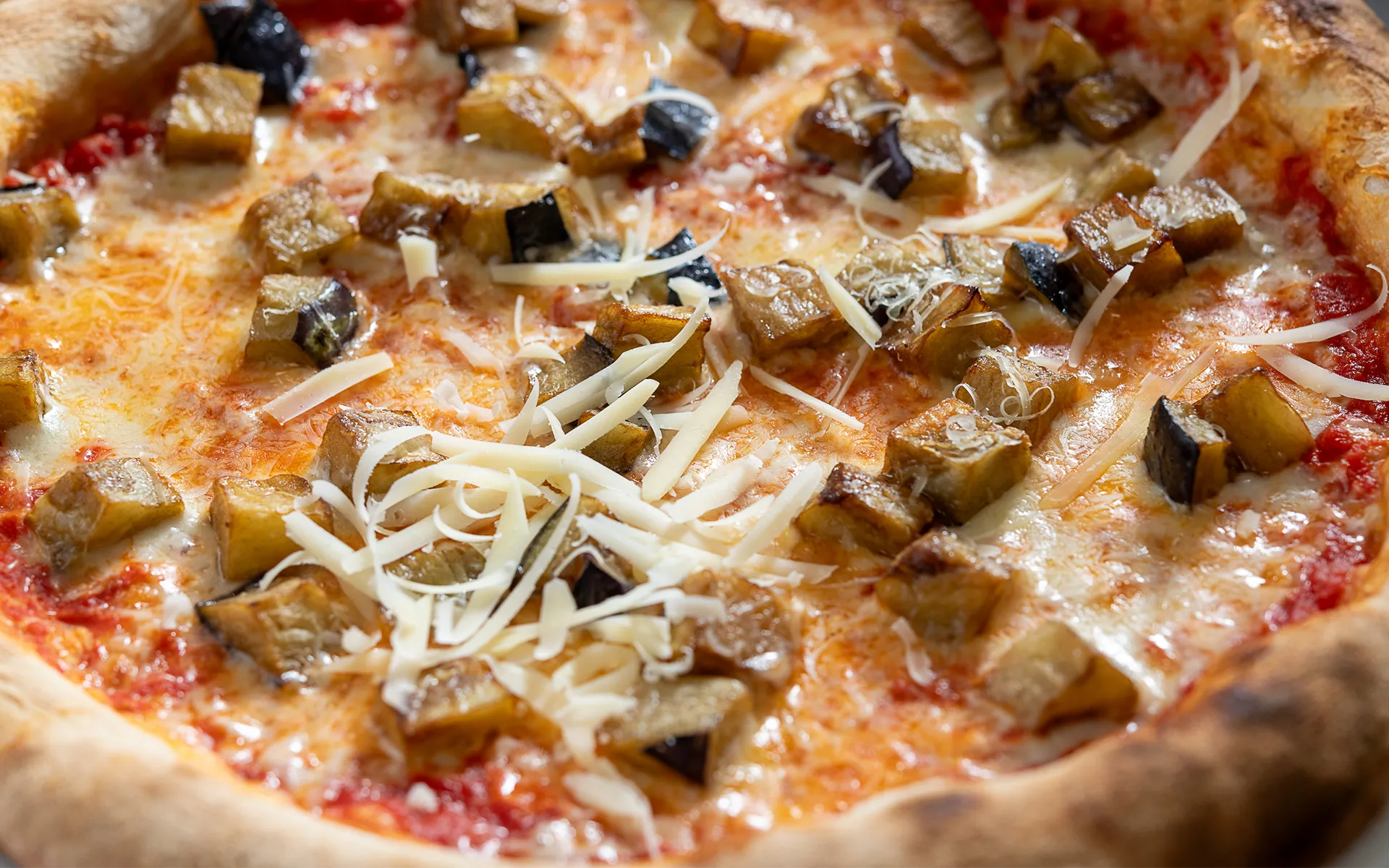 Pizza tonda con pomodoro, mozzarella filante e melanzane prefritte, dal gusto intenso e avvolgente.