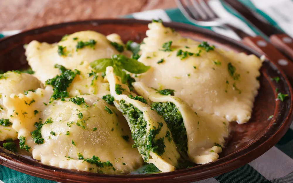 Raviolo Orogel agli spinaci, un classico ripieno verde, servito con formaggio e prezzemolo.
